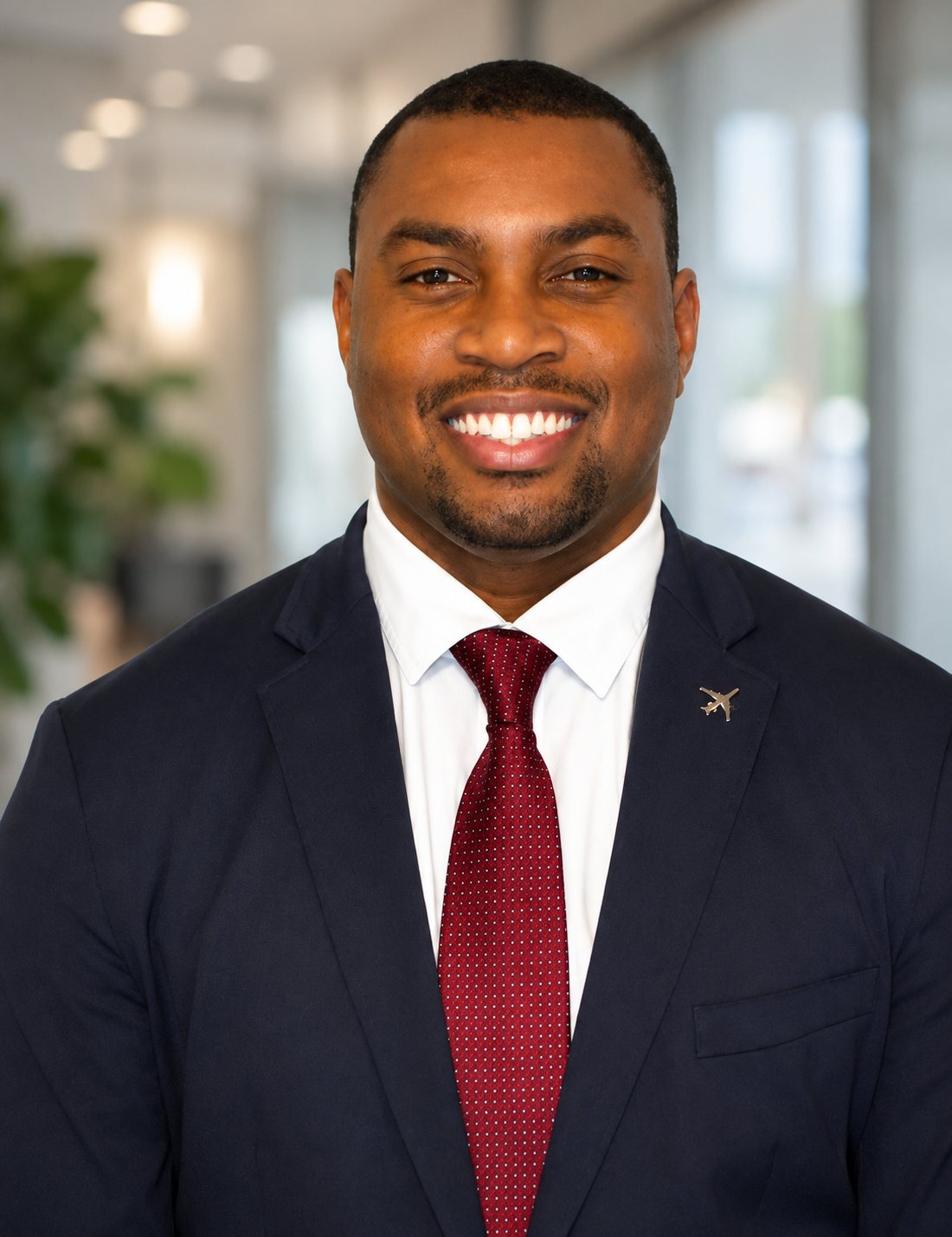 Cam Parker in a navy suit and red tie, wearing a gold airplane lapel pin, in a bright office